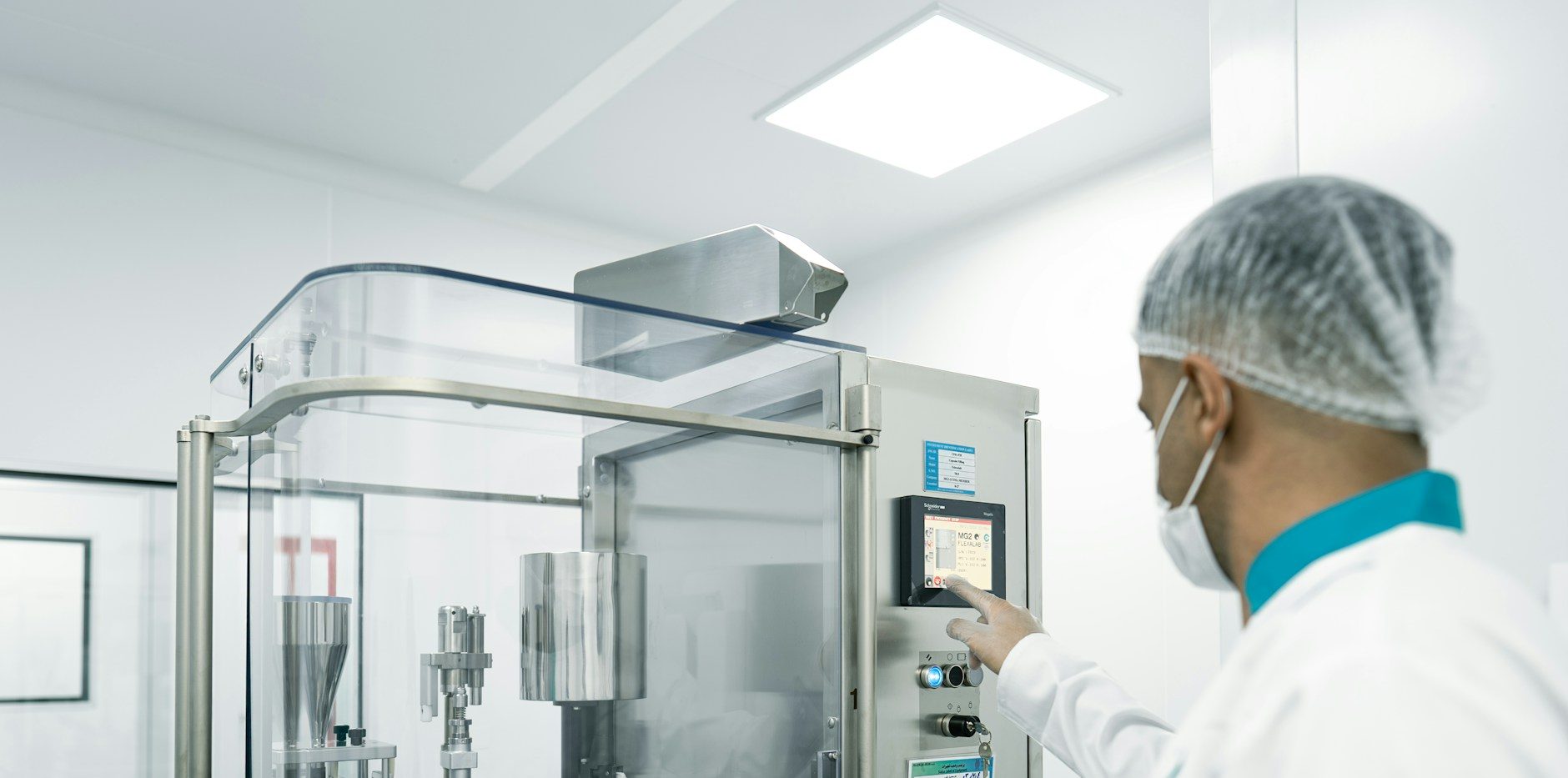 Operator in a hairnet and mask running a stainless filling line in a cleanroom