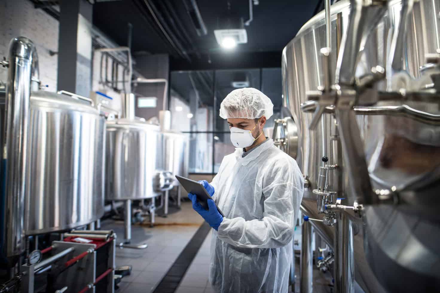 Operator in a cleanroom gown checking a step on a tablet at a filling line