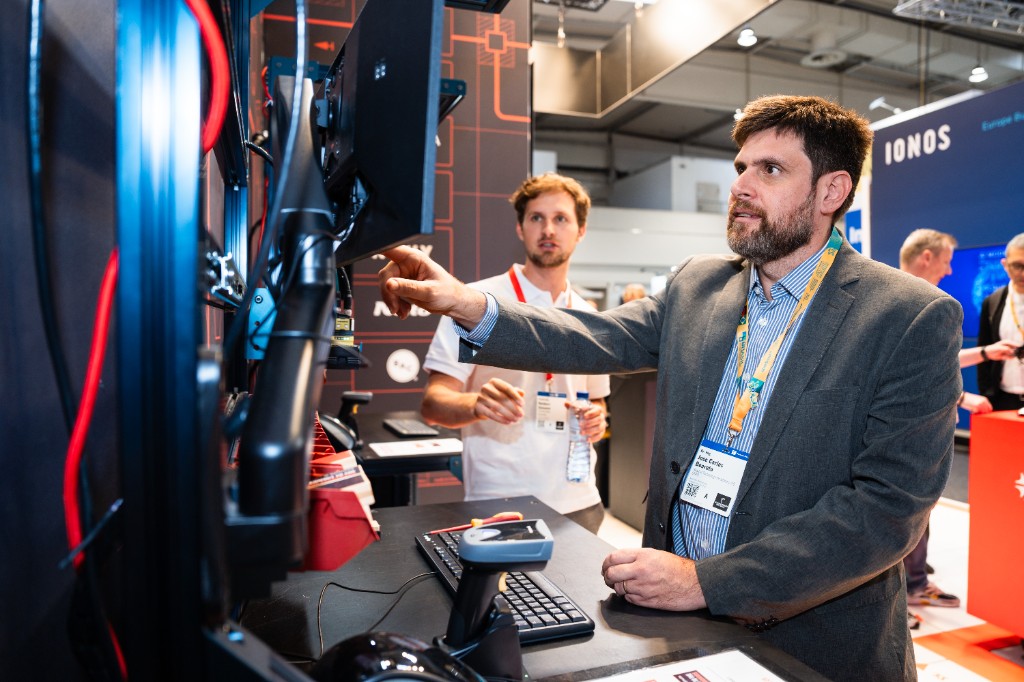 Een Azumuta-teamlid loopt met een bezoeker door het live operationele dashboard op het scherm op Hannover Messe 2026.