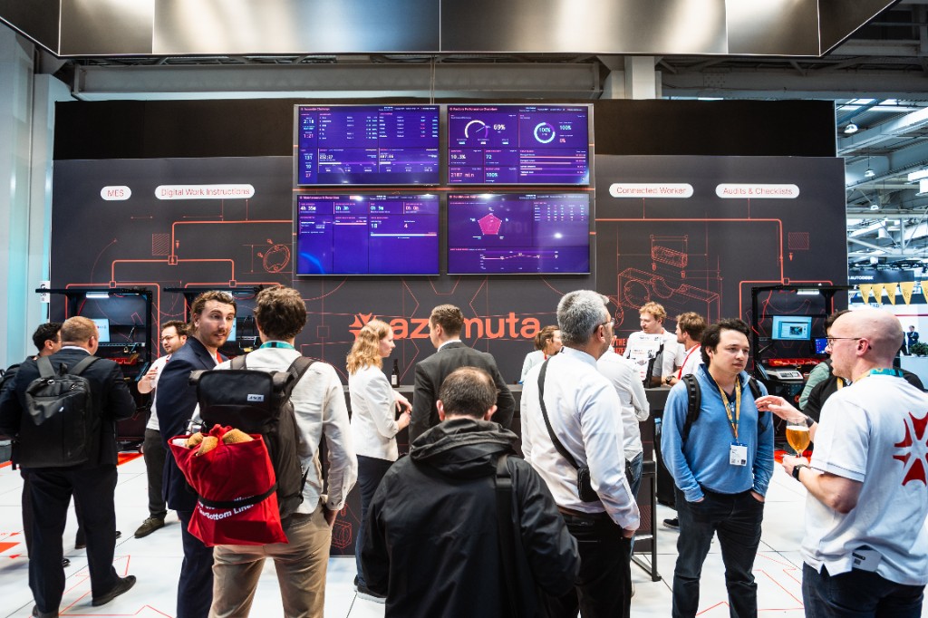 Een drukbezochte Azumuta-stand op Hannover Messe 2026, met bezoekers verzameld rond live dashboards op een wand vol schermen.